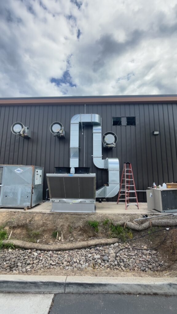 Commercial HVAC ventilation system with large metal ductwork and rooftop HVAC units installed on the exterior wall of a building.